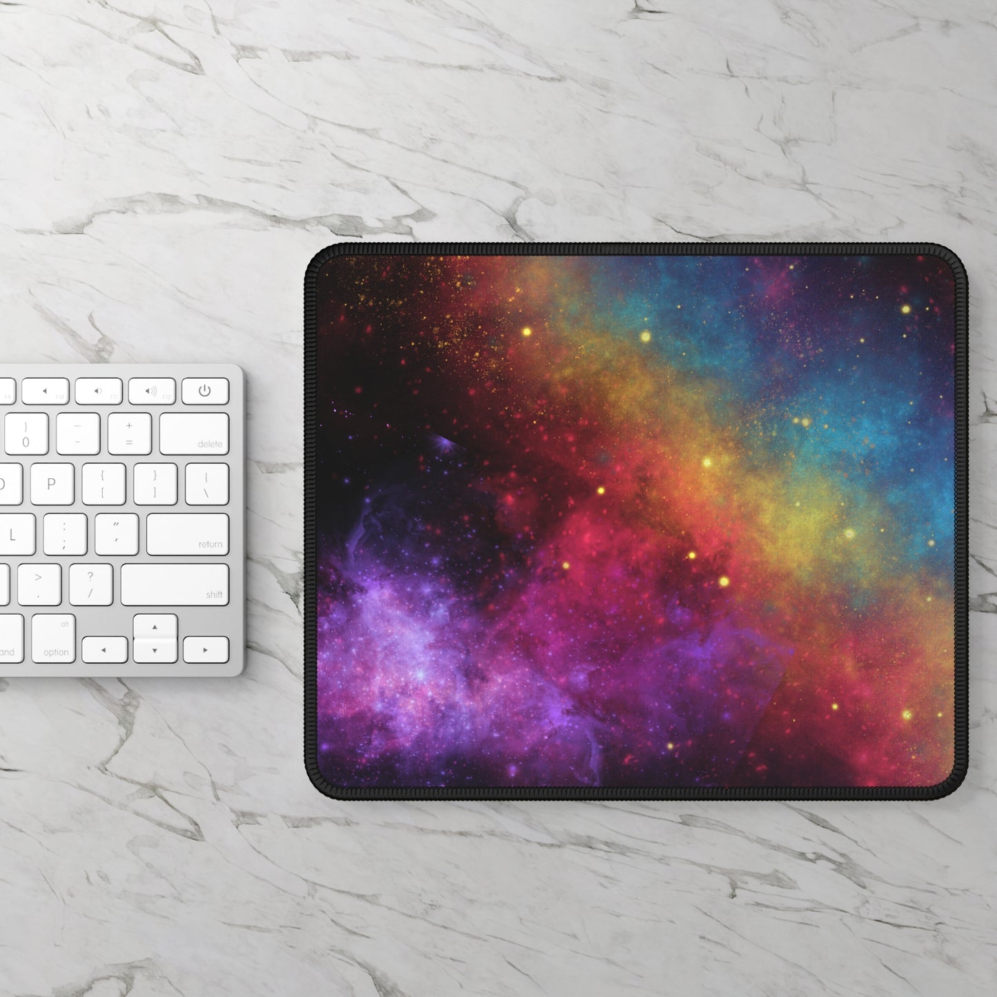 A white keyboard rests on marble beside the Printify Cosmic Galaxy Gaming Mouse Pad, featuring a vibrant space design in purple, pink, yellow, orange, and blue with a smooth surface and anti-slip rubber base.