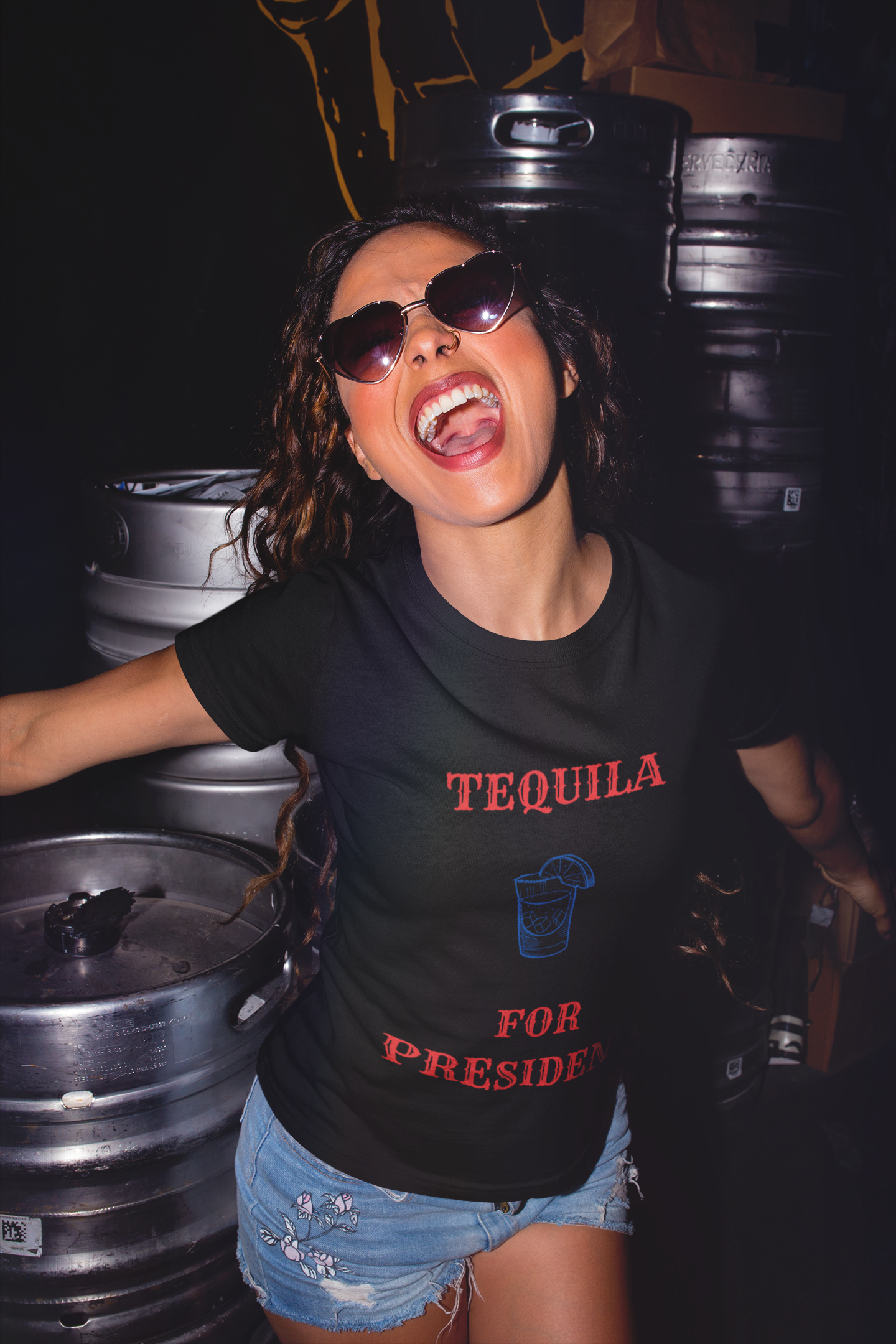 Smiling woman wearing Printify black tee with tequila for president political humor t-shirt design in bar with beer kegs