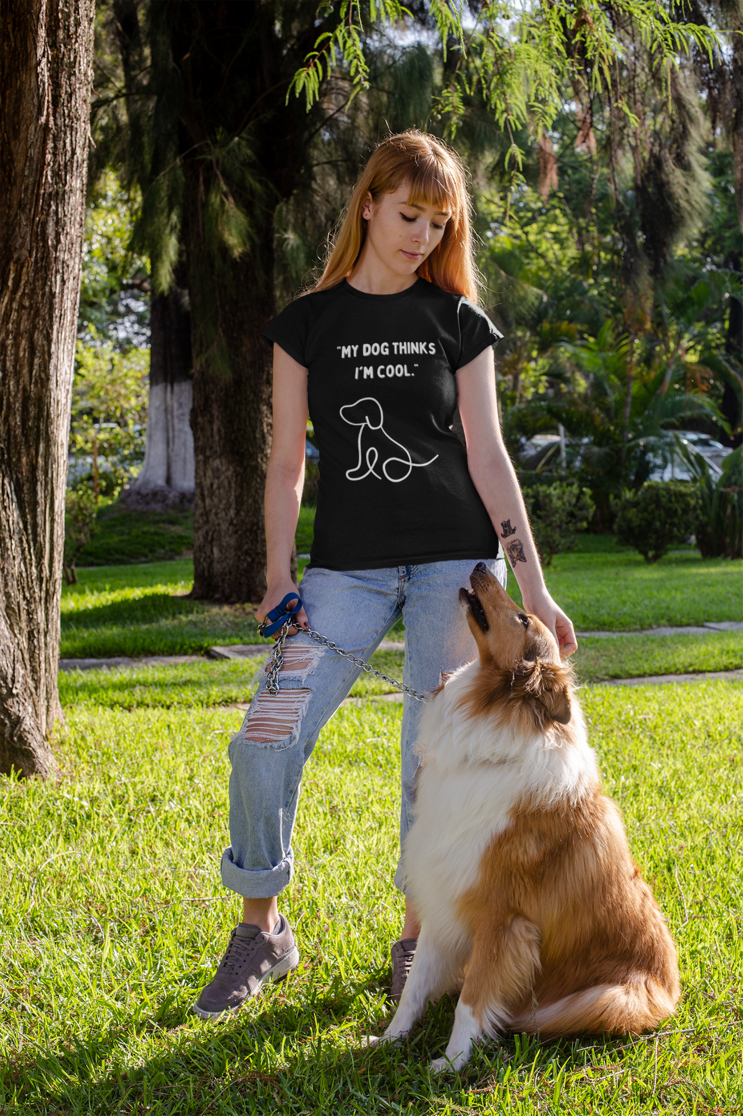 Woman wearing black funny dog lover t shirt with dog graphic standing in park with collie on leash and ripped jeans