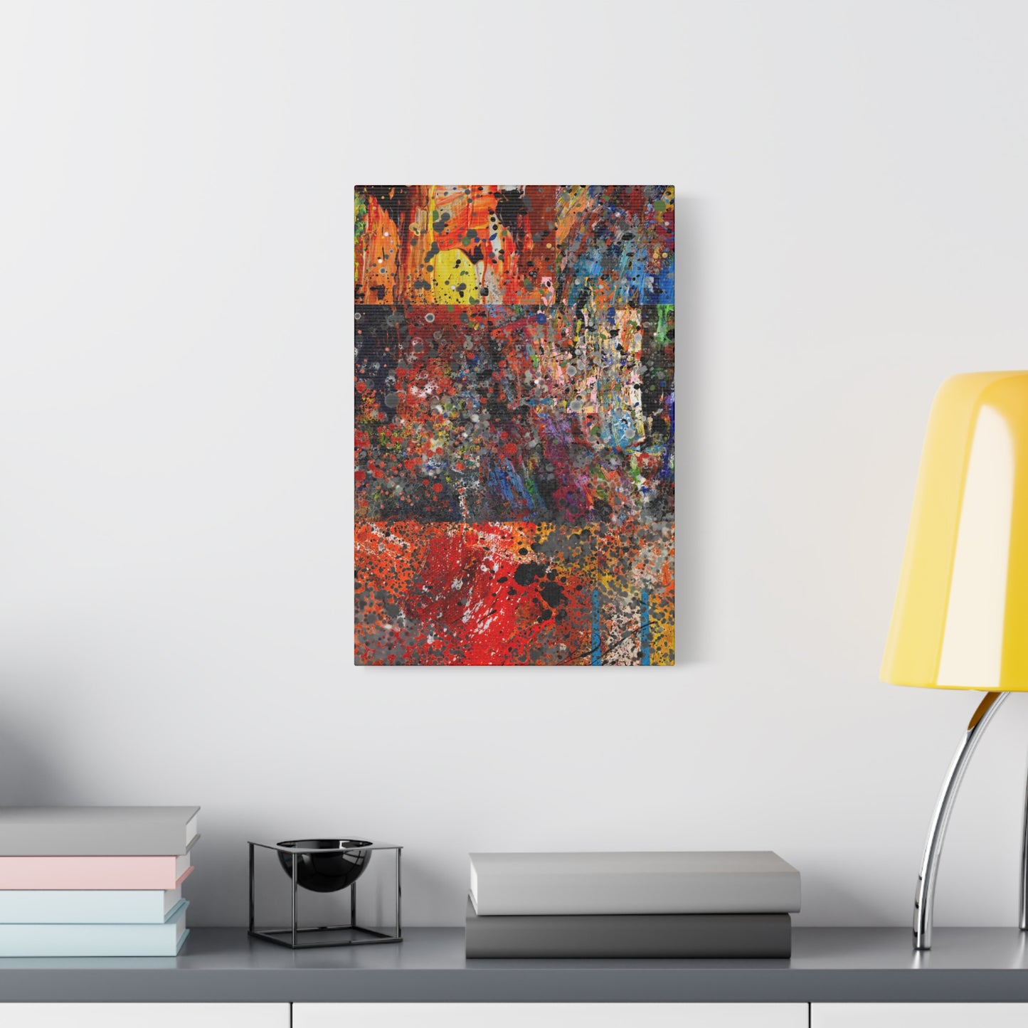 Red and orange abstract art canvas print hanging on white wall above desk next to yellow lamp and books