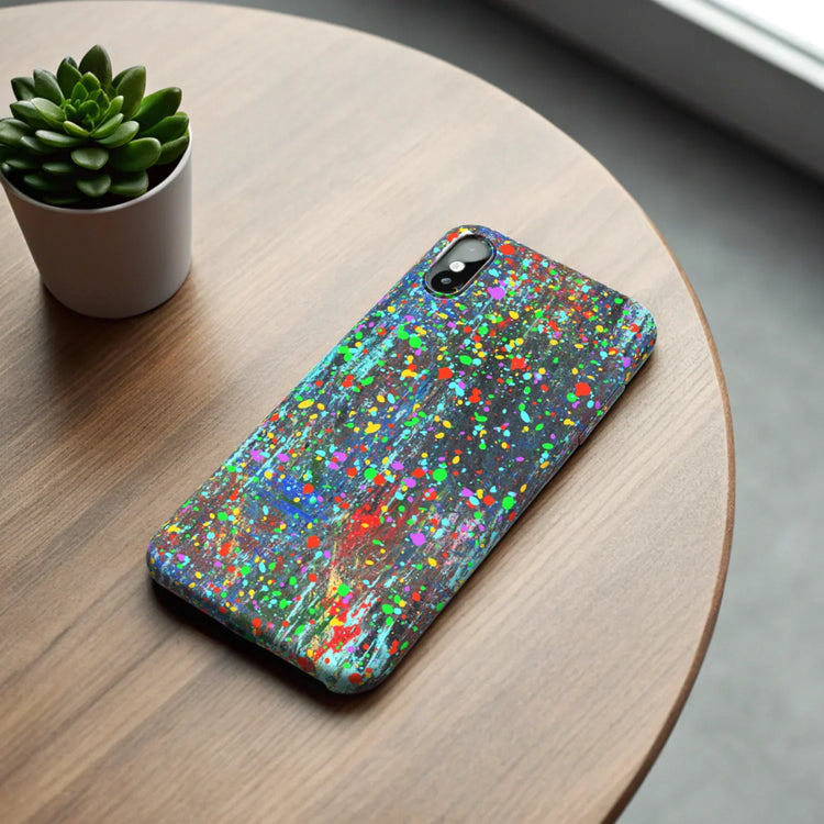 Quirky funny and artistic protective phone covers with colorful splatter design on wood table next to small green plant