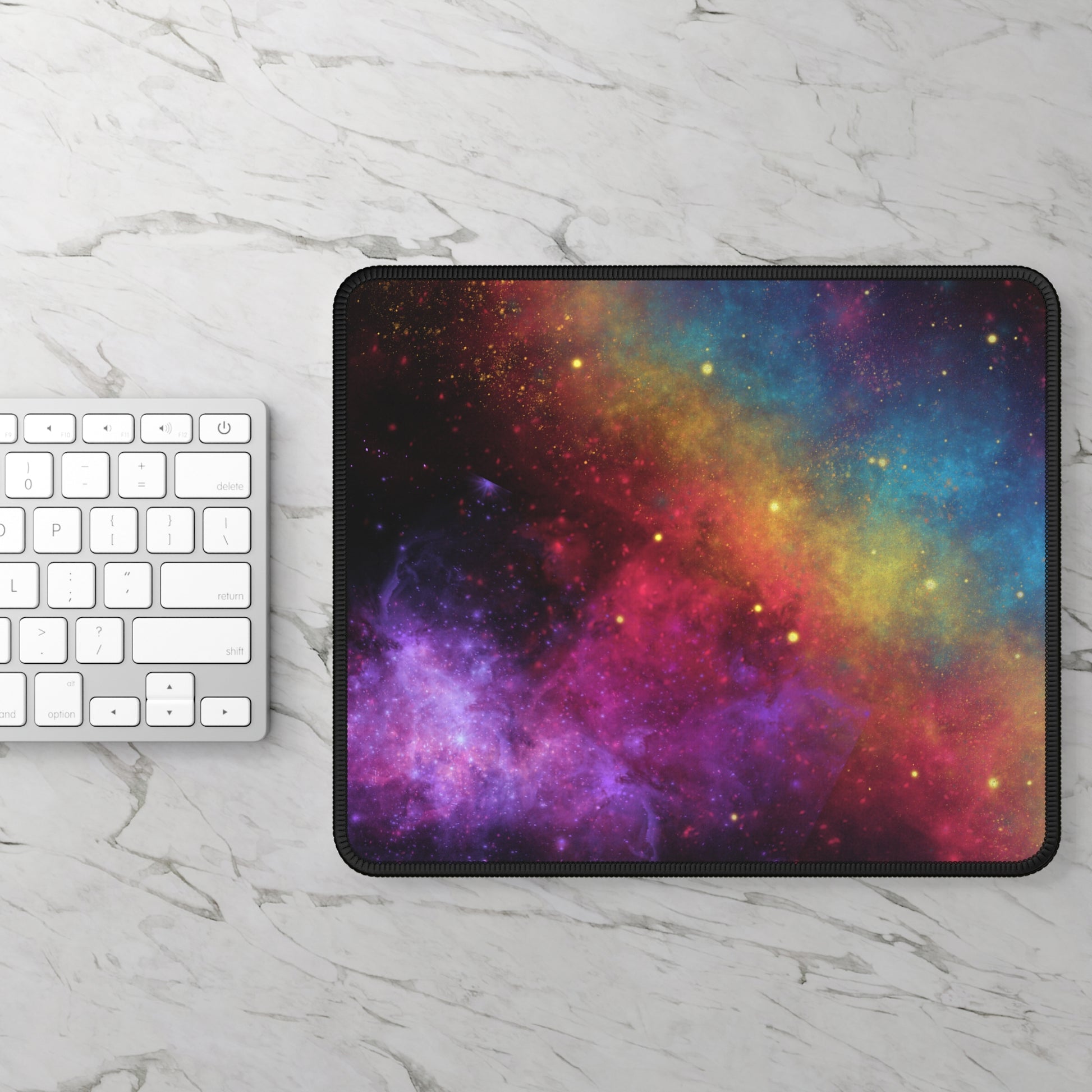 A white keyboard rests on marble beside the Printify Cosmic Galaxy Gaming Mouse Pad, featuring a vibrant space design in purple, pink, yellow, orange, and blue with a smooth surface and anti-slip rubber base.