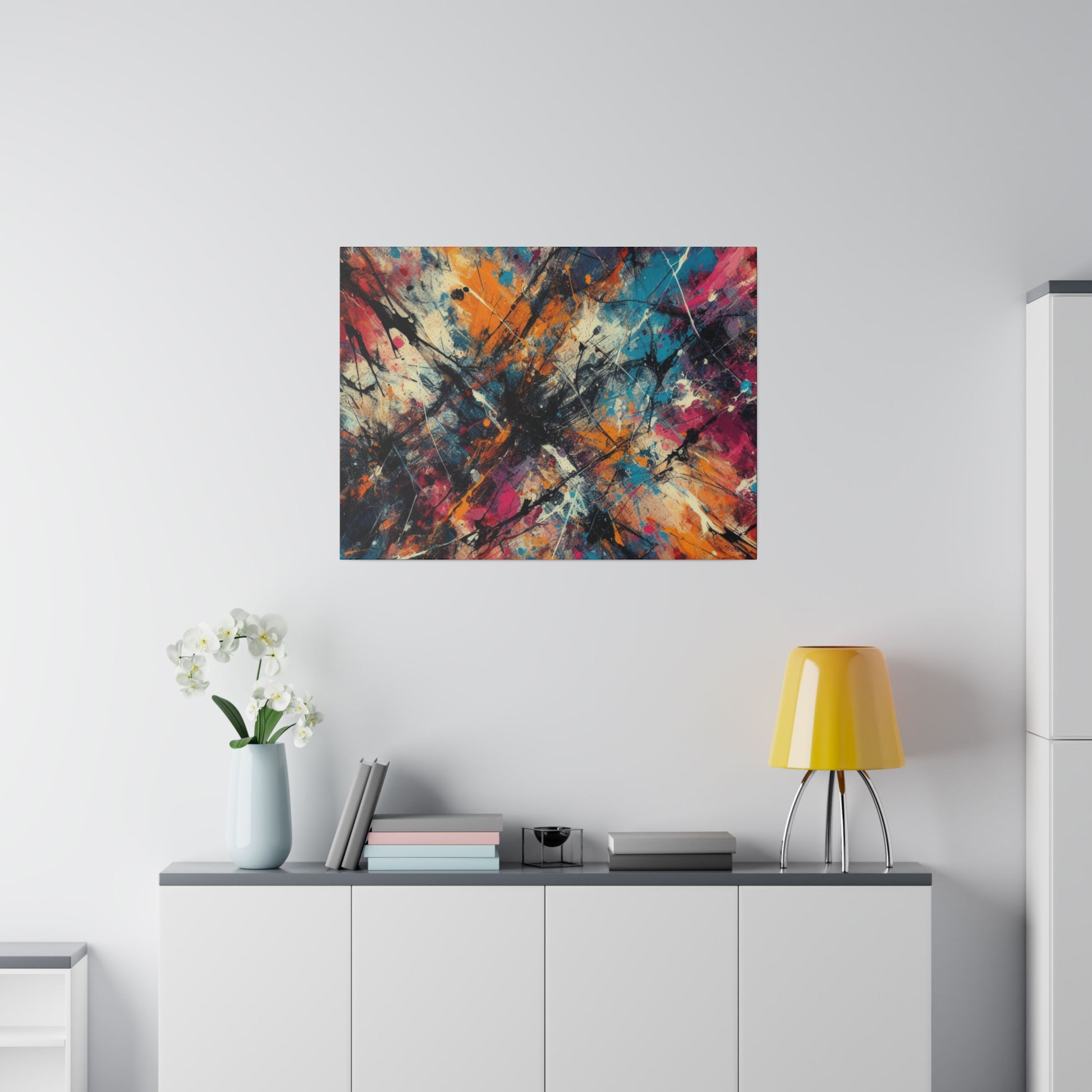 Printifys Abstract Geometric Canvas Print – Modern Wall Art Decor hangs on a light gray wall. Below, a modern white cabinet displays a vase with white flowers, some books, and a yellow lamp. The room exudes minimalism and brightness.