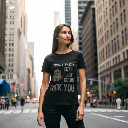 A confident woman stands on a city street in a Printify Funny Cat Graphic T-Shirt, featuring soft colors and bold text: Im Not Always a Bitch, Just Kidding, Fuck You, while tall buildings rise in the background.