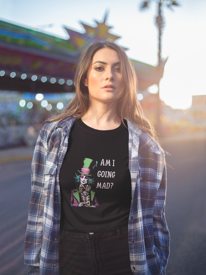 A woman with long brown hair stands near a bright amusement ride, wearing the Printify Unisex Garment-Dyed T-Shirt featuring a vintage-inspired Mad Hatter design and “Am I Going Mad?” text, layered under a plaid shirt.