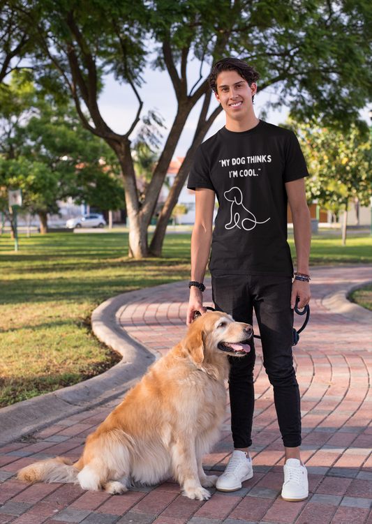 Man in park wearing a black funny dog lover t shirt reading My dog thinks Im cool while holding a golden retriever on leash