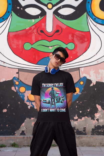 A young man in sunglasses and headphones stands before a vibrant mural, wearing the Printify Retro Graphic T-Shirt featuring the slogan Im Sorry Im Late, I Didnt Want to Come—a bold pick for pop culture fans.